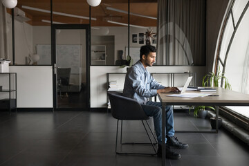Serious thoughtful Indian businessman, male office employee analyzing data, or writing emails,...
