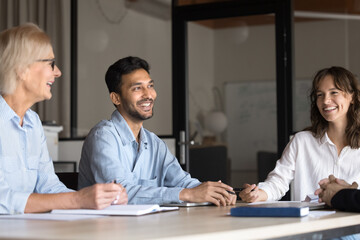 Happy teammates lead informal talk seated at conference table. Multiethnic businesspeople or...