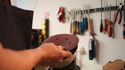 Craftsperson putting sandpaper discs on sander device to be used on smoothing wood surfaces. Woodworking expert preparing necessary gear for furniture assembling commission, close up, camera B