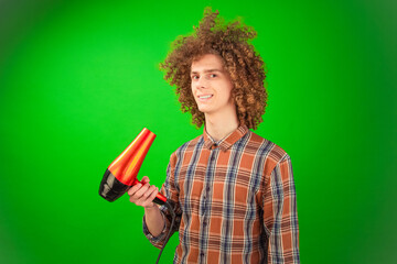 Standing confidently in front of the green Chroma Key, the curly-haired man channels a breeze through his hair and shirt using a hairdryer.
