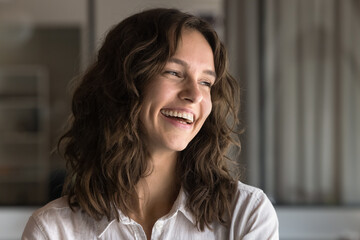 Close up face of laughing millennial 30s woman, looking away, having joyful expression, standing...