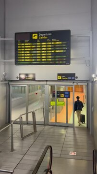 Traveler descending escalator in airport terminal towards departure gates, illuminated departure board, and modern interior design