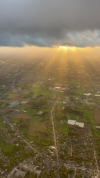 Aerial view of sunbeams breaking through dramatic clouds, illuminating lush green farmland and countryside below