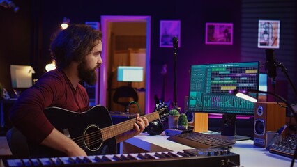Music producer mixing guitar sounds played by him on acoustic instrument, using electronic...