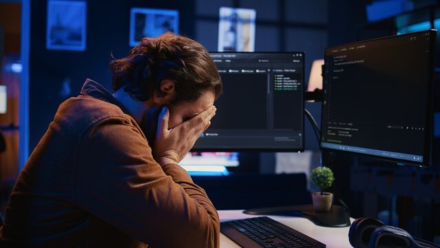 Annoyed software developer exasperated after failing to remove all bugs while coding on computer desktop. Teleworking IT specialist throwing keyboard, frustrated by script errors, camera B