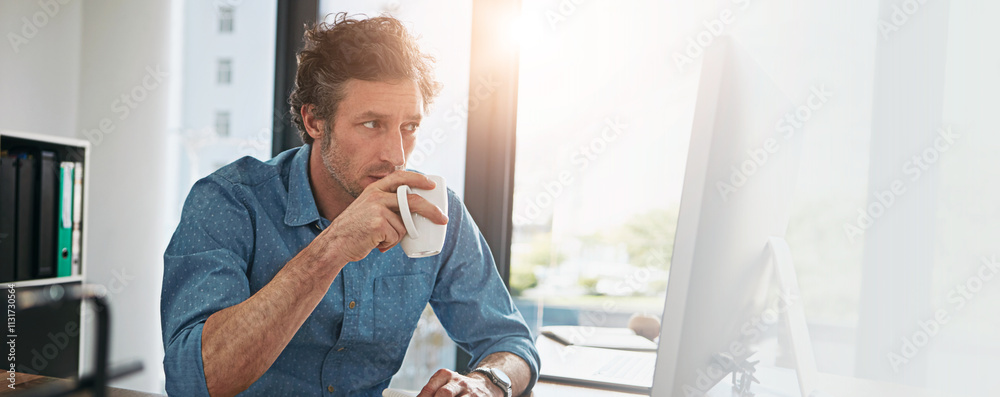 Poster computer, coffee and reading with designer man at desk in office for development, planning or resear