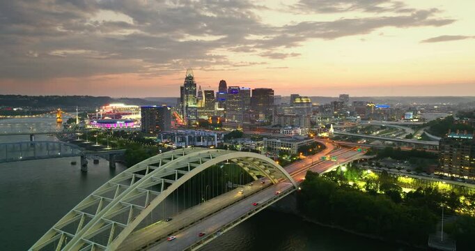 Highway traffic on bridge in Cincinnati, Ohio with illuminated skyscraper buildings in downtown district. American city with business financial district at sunset.