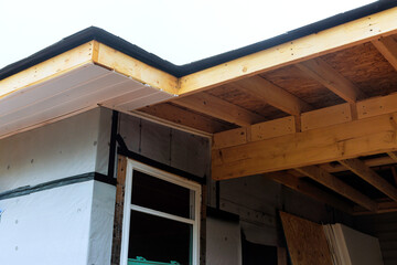 Construction are installing roofing materials on house, focusing on eave detailing improvements.