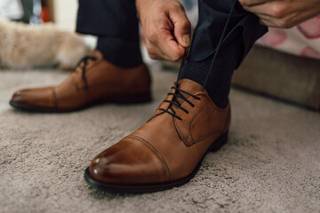 A close-up of polished brown leather dress shoes, with a hand tying the black laces. perfectly...