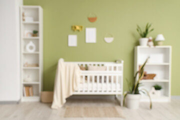 Fototapeta premium Beautiful crib with plaid and shelving unit near green wall in interior of children's room, blurred view