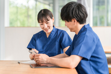 スマホを見ながら会話する先輩看護師と若い男性看護師
