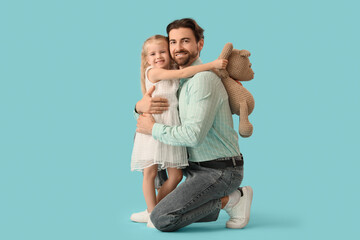 Cute little girl with toy bear hugging her father on blue background. International Hug Day
