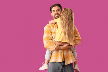 Young man holding his little daughter in arms on pink background