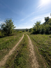 Idyllic countryside trail, wheel marks in grass, sunny day with hilly surroundings