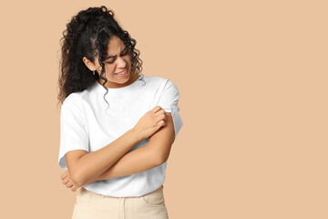 Young African-American woman suffering from skin allergy on beige background