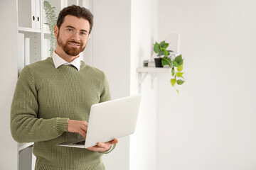 Handsome man working with laptop near shelf unit in office