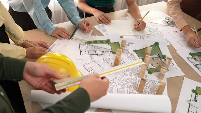 Architect and safety engineer discussion about building construction use blueprint on table with architectural document, measurement tool and wooden block scatter around at modern office. Delineation.