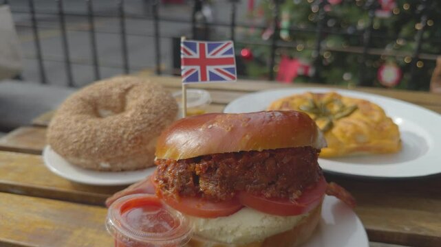 A cozy scene featuring an English bagel with a small British flag on a bagel, framed by a festive Christmas tree and a bustling street view in the background.