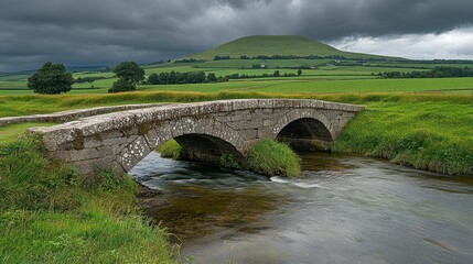 Fototapeta premium Stone bridge over stream, hill, and stormy sky.