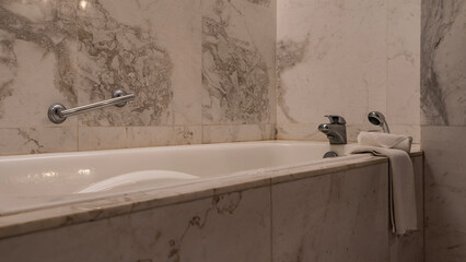 A fragment of the bathroom. A rectangular white bathtub in the corner against a beige tiled wall....