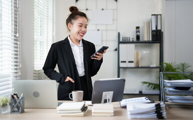 Naklejka premium Young busy business woman talking on phone working in modern office. Asian businesswoman company sales client manager wearing suit making call on cellphone Standing at workplace.