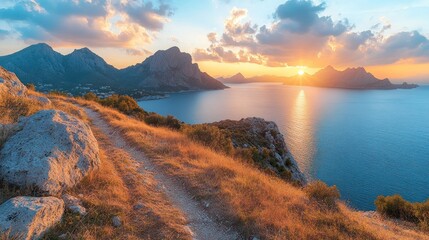 Fototapeta premium A panoramic view of a golden sunset over the ocean with mountains in the distance and a hiking trail leading to the peak.