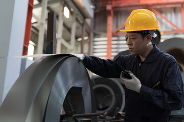 Asian male engineer inspecting quality rolls of galvanized or metal sheet. Male engineer working in...