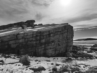 A solitary rock formation in black and white, set in a snowy field beneath a moody, overcast sky....