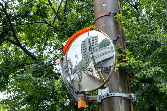 a safety convex mirror with curved surface mounted on a pole, offers a distorted view of the surrounding buildings in a residential neighbourhood street in Japan.