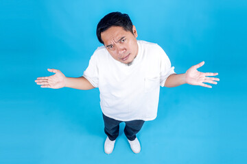 High Angle Portrait of Asian Clueless and Confused Man Shrugging Shoulders Isolated on Blue...