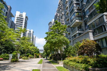 A paved walkway winds through the communal garden of a modern apartment complex in a densely populated Chinese neighborhood. Concept of real estate, living environment and housing market.