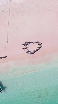 Aerial top drone view of people holding hands and enjoying holiday at Pink Beach Island in Labuan Bajo.