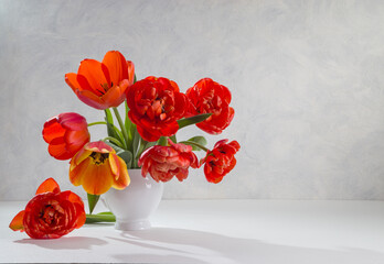 A bouquet of red tulips in a white vase on a light background. Copy space.
