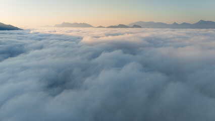 Fototapeta premium aerial overview of a sea of clouds glowing in golden hues during sunrise over hills