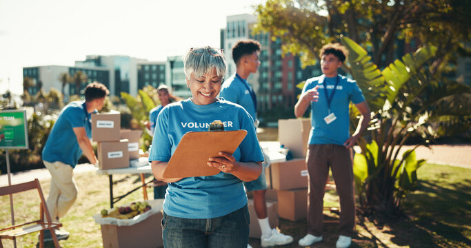 Happy, volunteers and mature woman with clipboard, charity and inventory for donations, smile and ngo. Outdoor, team and coordinator with checklist for info, community service and boxes for nonprofit - Powered by Adobe
