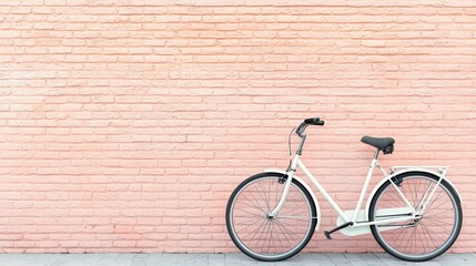 Fototapeta premium Old-school and retro simplicity, A vintage white bicycle leans against a soft pink brick wall, creating a charming and minimalist aesthetic.