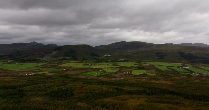 Sortland Northern Norway landscape with lush green fields and mountains rising in the distance under overcast sky, aerial establish approach