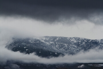 Snow covered hilltop with black storm clouds approaching in the foreground. Ominous weather.
