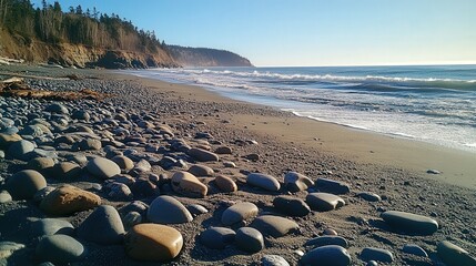A rocky beach with smooth pebbles scattered across the shore, the sun casting long shadows over the stones as the ocean churns in the distance.