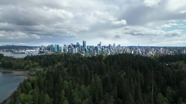 aerial shot over stanley park revealing vancouver city skyline on a cloudy day, british columbia, canada