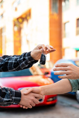 Salesman giving car key to customer and shaking hands in front of new car, closing a deal