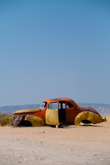 Vintage car abandoned in Solitaire, Namibia. Its rusty yellow and orange hues contrast with the arid sands and blue sky, reflecting nostalgia and the passage of time