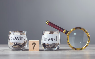 Man holding a magnifying glass near two glass jars filled with coins, one labeled Saving and the...