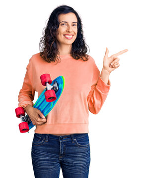 Young beautiful hispanic woman holding skate smiling happy pointing with hand and finger to the side