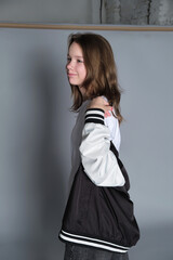 A young girl looks over her shoulder with a gentle expression, her jacket loosely draped around...