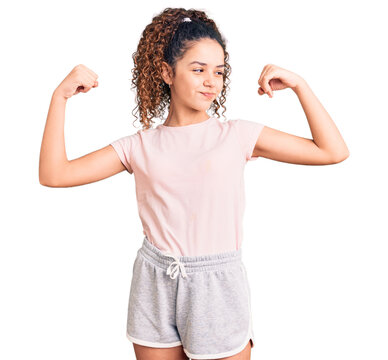 Beautiful kid girl with curly hair wearing casual clothes showing arms muscles smiling proud. fitness concept.