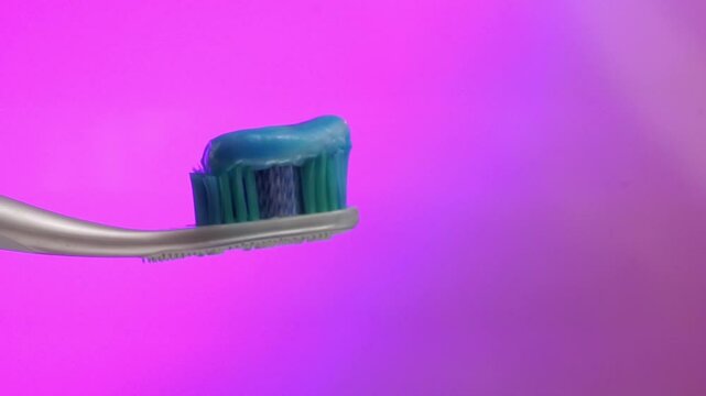 Close-up of a toothbrush with toothpaste on its blue bristles, with a purple blurred background