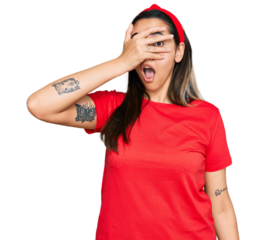 Young hispanic woman wearing casual clothes peeking in shock covering face and eyes with hand, looking through fingers with embarrassed expression.