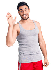 Fototapeta premium Young handsome man wearing swimwear and sleeveless t-shirt waiving saying hello happy and smiling, friendly welcome gesture