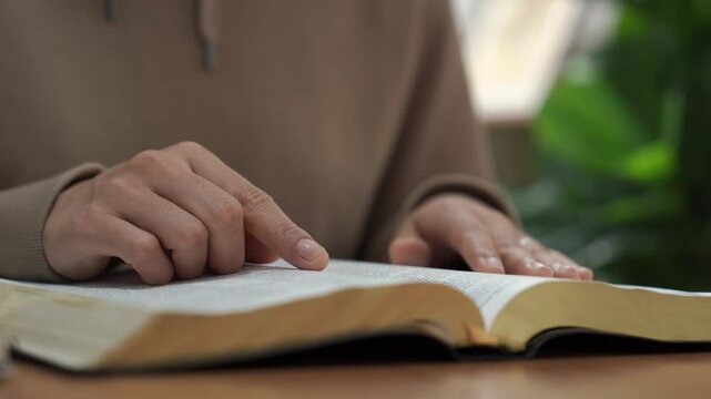 Christian hand, book and bible study at home for religion learning on spiritual scripture for pray and worship. Person search for inspiration in gospel